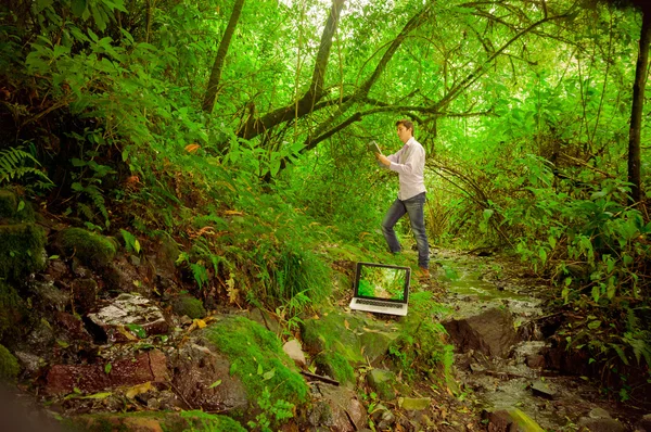 Mladý pohledný muž pomocí tabletu a notebook s velkou připojení k Internetu v džungli — Stock fotografie