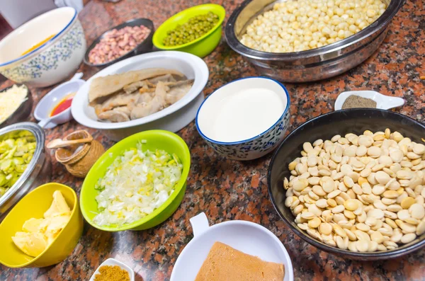 Bowls of different ingredients spread out on granite surface including green peas, onions, abbas, corn, fish, lupini and red beans — Stock Image Bowls of different ingredients spread out on granite surface including green peas, onions, abbas, corn, fish, lupini and red beans Stock Photo