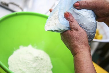 Two hands holding bag of flour while puring into green plastic bowl, preparing fanesca concept