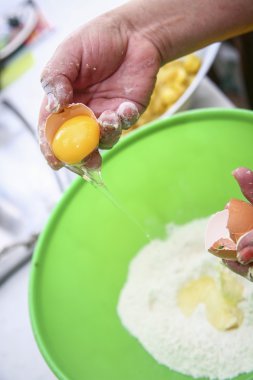 Two hands separating eggwhite from yolk over green plastic bowl of flour, preparing fanesca concept