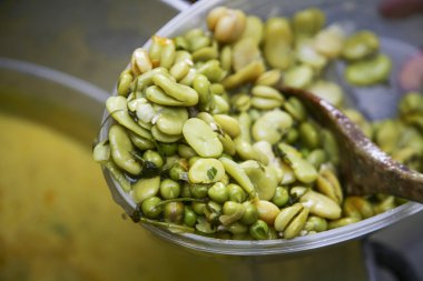 Closeup bowl of cooked abbas with wooden spoon lying inside, preparing fanesca concept