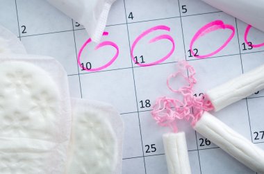 White calendar with pink circles around menstruation date period and clean tampons lying on top clipart