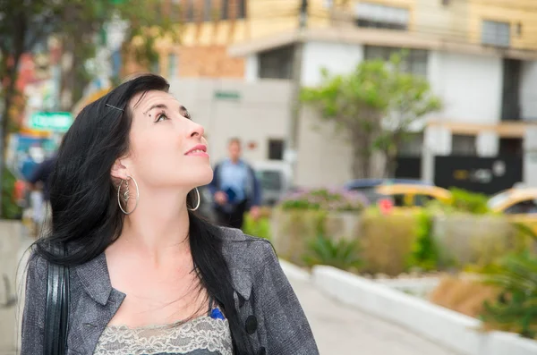 Classy latina model wearing smart casual clothes walking in urban street looking upwards and smiling — 스톡 사진