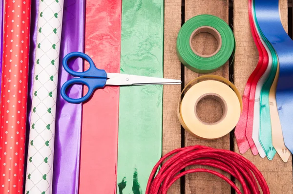 Geschenkverpackungskonzept mit verschiedenen Papierfarben, Scheren, Klebeband und anderen Dekorationen auf Holzoberfläche liegend — Stockfoto