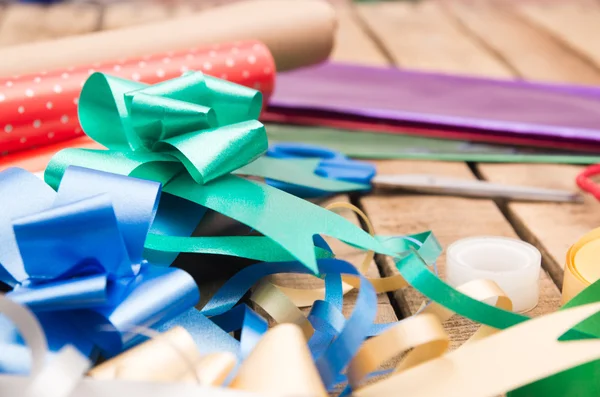 Concepto de envoltura de regalo con varios colores de papel, tijeras, cinta adhesiva y otros decorativos que yacen en la superficie de madera —  Fotos de Stock