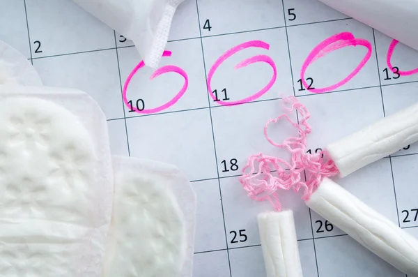 Белый календарь с розовыми кругами вокруг периода менструации даты и чистые тампоны лежащие сверху — стоковое фото
