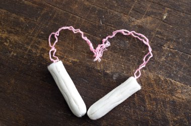 Two clean white tampons shaped in to a heart lying on wooden surface clipart