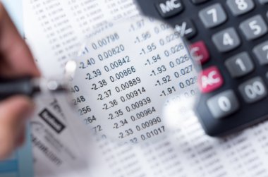 Closeup magnifying glass over paper with numbers and calculator sitting besides