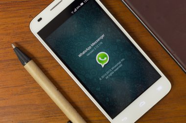 QUITO, ECUADOR - AUGUST 3, 2015: White smartphone lying on wooden desk with screen activated displaying WhatsApp next to a pen, business and communication concept