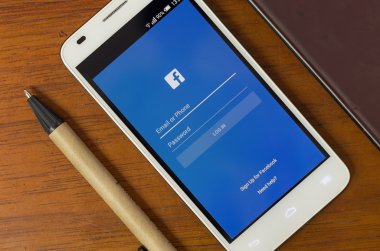 QUITO, ECUADOR - AUGUST 3, 2015: White smartphone lying on desk with Facebook screen open next to a pen, business and communication concept