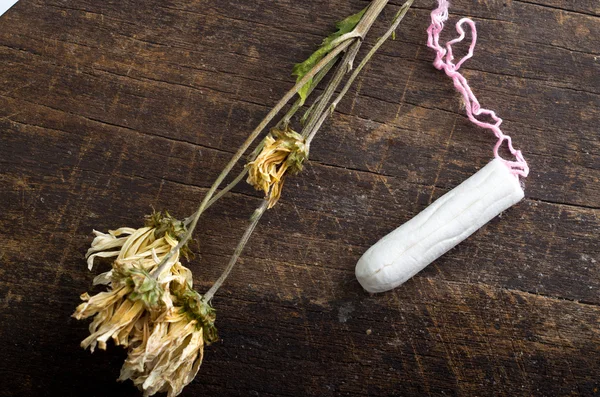 Clean white tampons lying on wooden surface with yellow colored dry flowers around — ストック写真