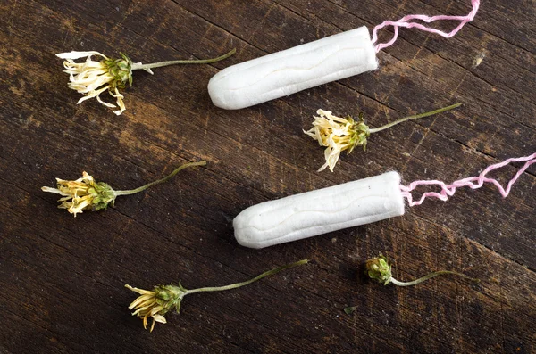 Clean white tampons lying on wooden surface with yellow colored dry flowers around — Zdjęcie stockowe