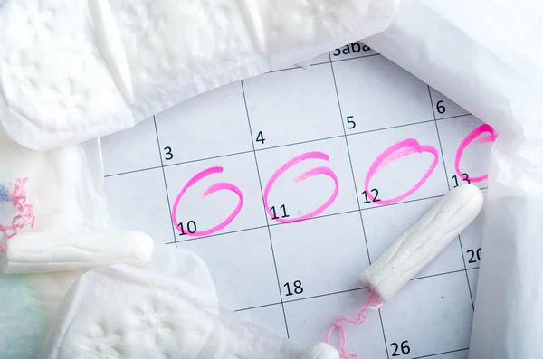 Calendario blanco con círculos rosados alrededor del período de la fecha de menstruación y tampones limpios acostados en la parte superior —  Fotos de Stock