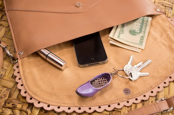 Womans purse beige color lying flat with accessories such as mobile, makeup, keys and money spread out in front — 图库照片
