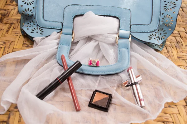 Womans purse light blue color lying flat with accessories such as mobile, makeup, keys and money spread out in front