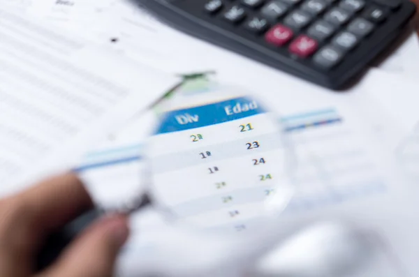 Closeup magnifying glass over paper with numbers and calculator sitting besides — Stock fotografie