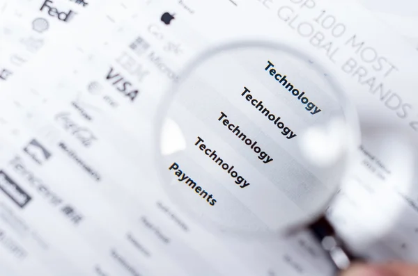 Closeup magnifying glass over paper with the words technology and payment visible — стокове фото