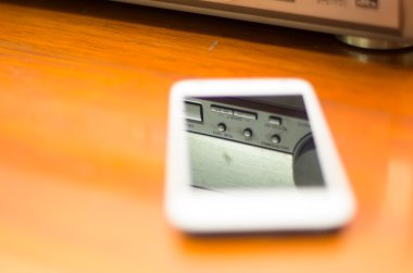 QUITO, ECUADOR - AUGUST 3, 2015: White smartphone lying on wooden desk with reflection of stereo in screen, business communication concept