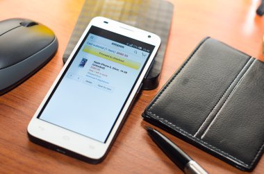 QUITO, ECUADOR - AUGUST 3, 2015: White smartphone lying on wooden desk with Amazon website screen next to a pen, wallet and mouse, business communication concept