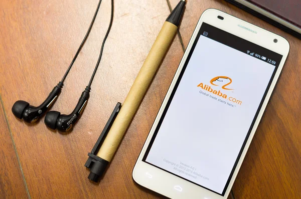 QUITO, ECUADOR - AUGUST 3, 2015: White smartphone lying on desk with Alibaba screen open next to a pen and headphones, business communication concept — Stock Photo, Image