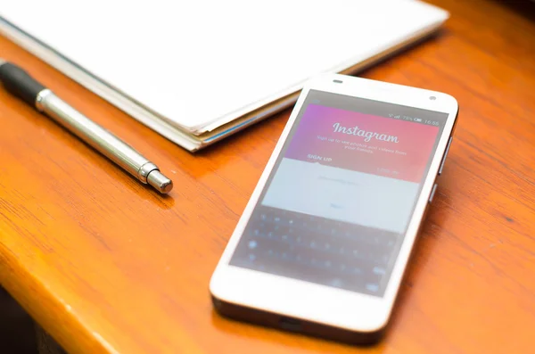 QUITO, ECUADOR - AUGUST 3, 2015: White smartphone lying on wooden desk with Instagram website screen next to a pen and notepad, business communication concept — Stockfoto