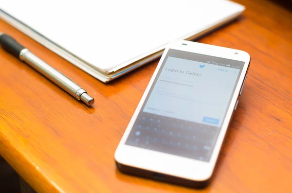 QUITO, ECUADOR - 3 августа 2015 года: Белый смартфон лежит на деревянном столе с экраном веб-сайта Twitter рядом с ручкой и блокнотом, концепция делового общения — стоковое фото