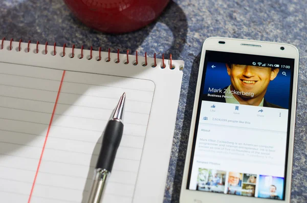 QUITO, ECUADOR - AUGUST 3, 2015: White smartphone lying on table with Facebook website screen open next to a pen, notepad and coffee mug, business communication concept — 图库照片