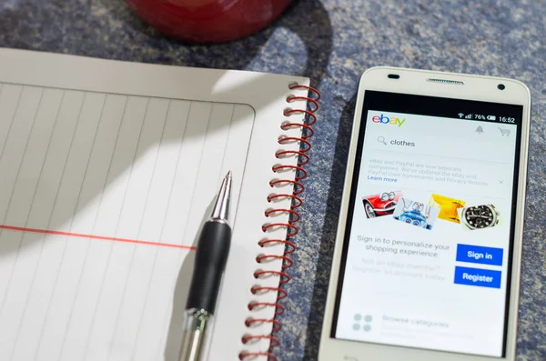 QUITO, ECUADOR - AUGUST 3, 2015: White smartphone lying on table with Ebay website screen open next to a pen, notepad and coffee mug, business communication concept — 图库照片