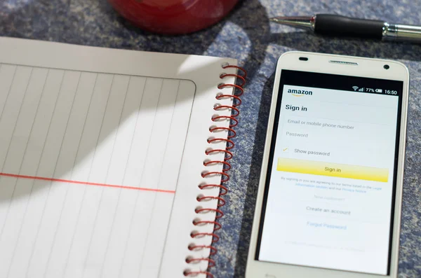 QUITO, ECUADOR - AUGUST 3, 2015: White smartphone lying on table with Amazon website screen open next to a pen, notepad and coffee mug, business communication concept — 图库照片