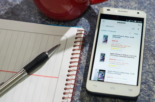 QUITO, ECUADOR - AUGUST 3, 2015: White smartphone lying on table with Amazon website screen open next to a pen, notepad and coffee mug, business communication concept — Stok fotoğraf