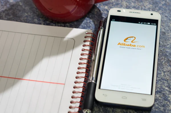 QUITO, ECUADOR - 03 de agosto de 2015: Smartphone branco deitado na mesa com tela do site Alibaba aberto ao lado de uma caneta, bloco de notas e caneca de café, conceito de comunicação de negócios — Fotografia de Stock
