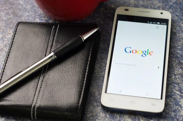 QUITO, ECUADOR - AUGUST 3, 2015: White smartphone lying on table with Google website screen open next to a pen, notepad and coffee mug, business communication concept — Stok fotoğraf