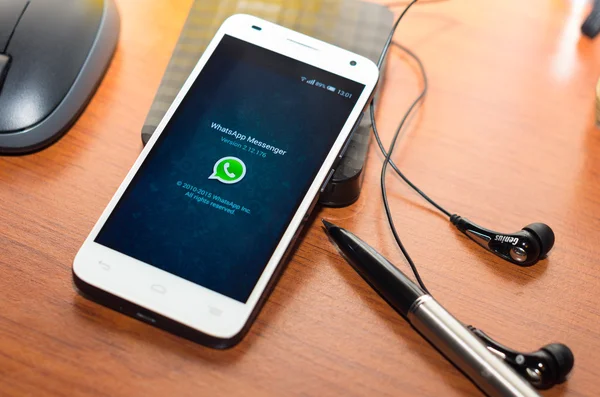 QUITO, ECUADOR - AUGUST 3, 2015: White smartphone lying on wooden desk with WhatsApp website screen next to a pen, headphones and mouse, business communication concept — 图库照片