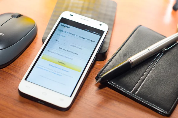 QUITO, ECUADOR - AUGUST 3, 2015: White smartphone lying on wooden desk with Amazon website screen next to a pen, wallet and mouse, business communication concept — Stock Photo, Image