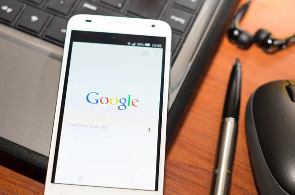 QUITO, ECUADOR - AUGUST 3, 2015: White smartphone closeup lying on laptop corner with Google website screen visible, eaplugs mouse and pen blurry background, business communication concept — ストック写真