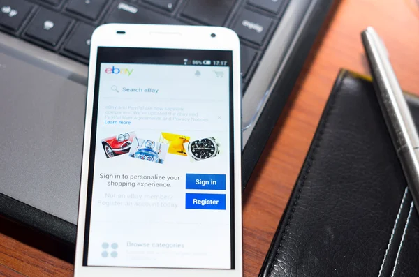 QUITO, ECUADOR - AUGUST 3, 2015: White smartphone closeup lying on laptop corner with Ebay website screen visible, eaplugs mouse and pen blurry background, business communication concept — Stock Photo, Image