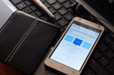 Quito, Ekvator - 3 Ağustos 2015: gümüş kalem ve m-cüzdan dizüstü klavye yanında Netflix Web sitesi giriş ekranı ile görünür yalan beyaz smartphone portre