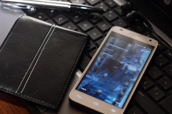 厄瓜多尔基多-2015年8月3日: 白色智能手机特写镜头位于笔记本电脑键盘上的银笔和钱包旁边, 可见未知的网站登录屏幕 — 图库照片