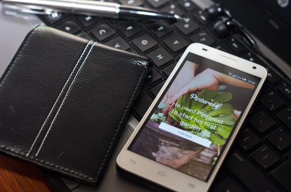 QUITO, ECUADOR - 3 de agosto de 2015: Primer plano del smartphone blanco junto a la pluma plateada y la billetera en el teclado del portátil con la pantalla de inicio de sesión del sitio web de Pinterest visible —  Fotos de Stock