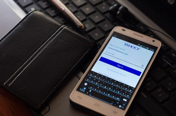 QUITO, ECUADOR - AUGUST 3, 2015: White smartphone closeup lying next to silver pen and wallet on laptop keyboard with Yahoo website login screen visible — стокове фото