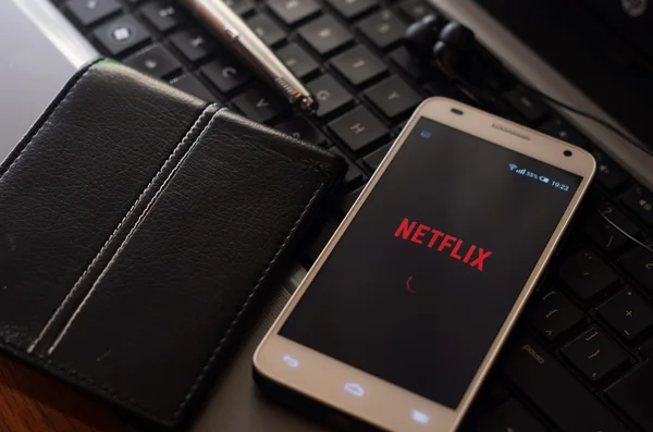 Quito, Ecuador - augusti 3, 2015: Vit smartphone närbild liggande bredvid silver penna och plånbok på laptop tangentbord med Netflix webbplats inloggningsskärmen synliga — Stockfoto