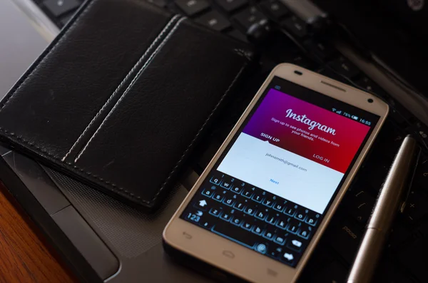 QUITO, ECUADOR - AUGUST 3, 2015: White smartphone closeup lying next to silver pen and wallet on laptop keyboard with Instagram login website visible screen — 图库照片