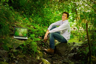 Laptop ile çalışma ve ormanda rahatlatıcı genç yakışıklı adam