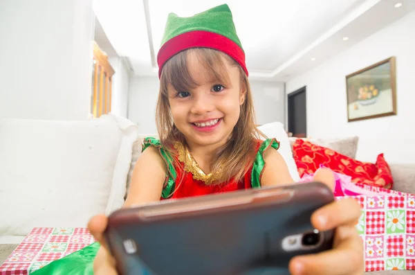 Joyeux petite fille habillée en robe de Noël tenant téléphone mobile — Photo