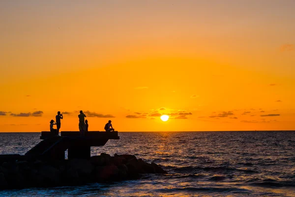 Sillhouette de personas en la playa durante la puesta del sol — Foto de Stock
