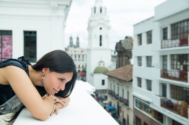 Classy attractive brunette wearing black white dress in urban environment leaning on surface and enjoying a view while looking thoughtful