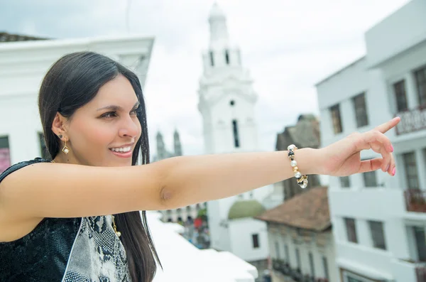 Classy attractive brunette wearing black white dress in urban environment leaning on surface enjoying a view while smiling and pointing — Stock Photo, Image