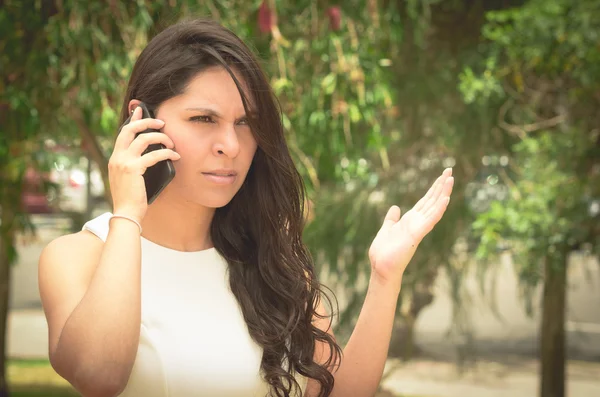 Classy attractive brunette wearing white dress talking on the phone in outdoors environment — Stok fotoğraf