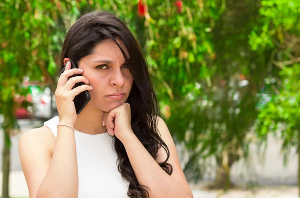 Classy attractive brunette wearing white dress talking on the phone in outdoors environment — Stok fotoğraf