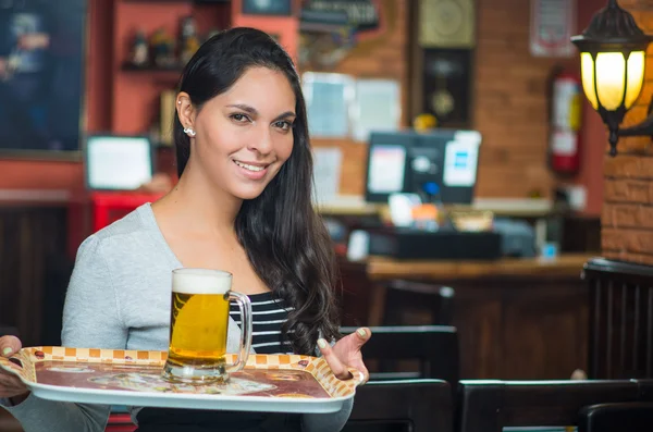 Brunette model serveerster in restaurant glimlachend gelukkig uitvoering een dienblad met glas fo bier op het — Stockfoto